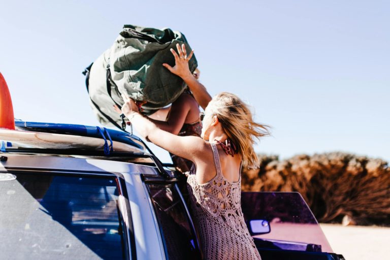 women throwing bag on roof of car